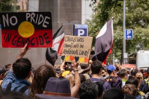 Australians protesting on the CBD streets, holding signs that say "no pride in genocide" and "always was always will be, aboriginal land"